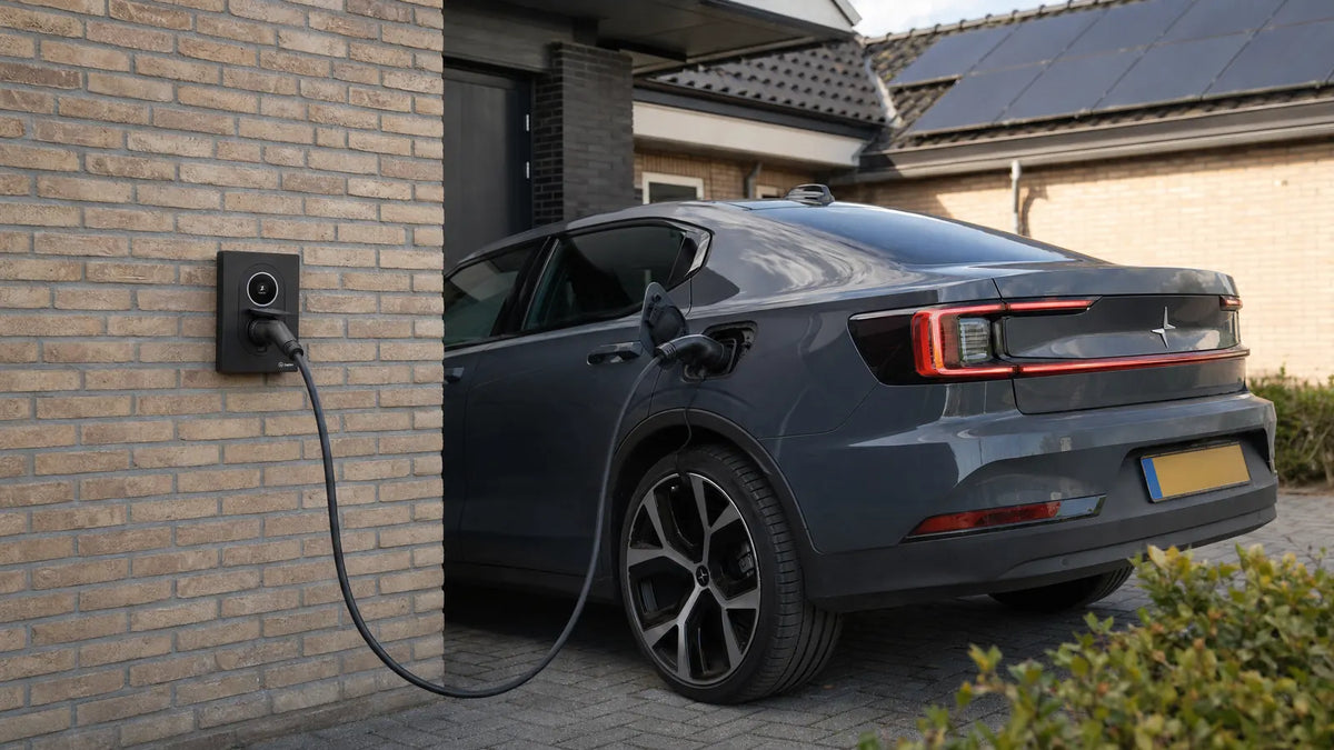 Laadpaal aan de gevel van een woning die met een losse laadkabel een elektrische auto op de oprit laadt