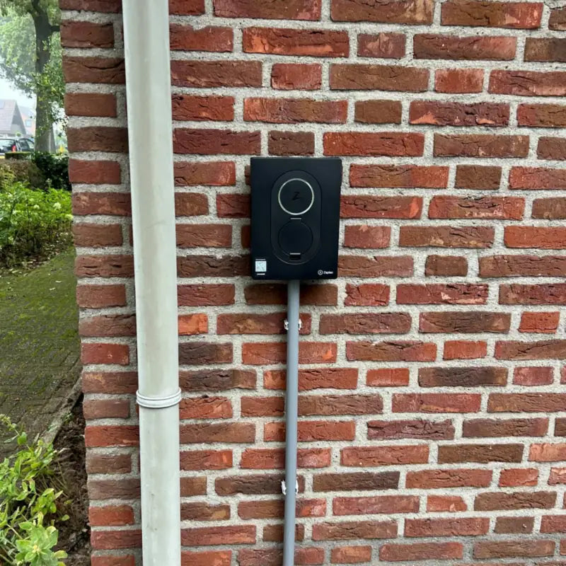 Zwarte Zaptec Go laadpaal gemonteerd aan een rode bakstenen muur naast de regenpijp